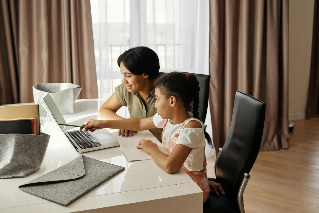 A mother and her daughter are working together on a laptop, focusing on homework