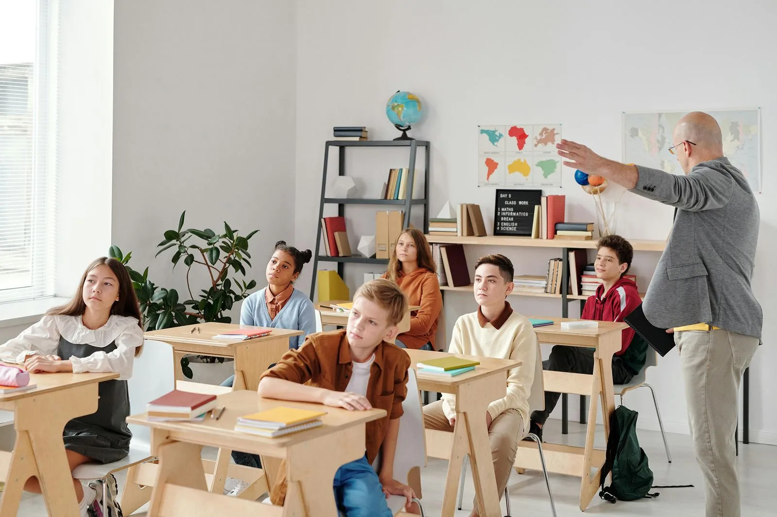 A teacher is explaining a topic to the class, speaking with gestures to emphasize points