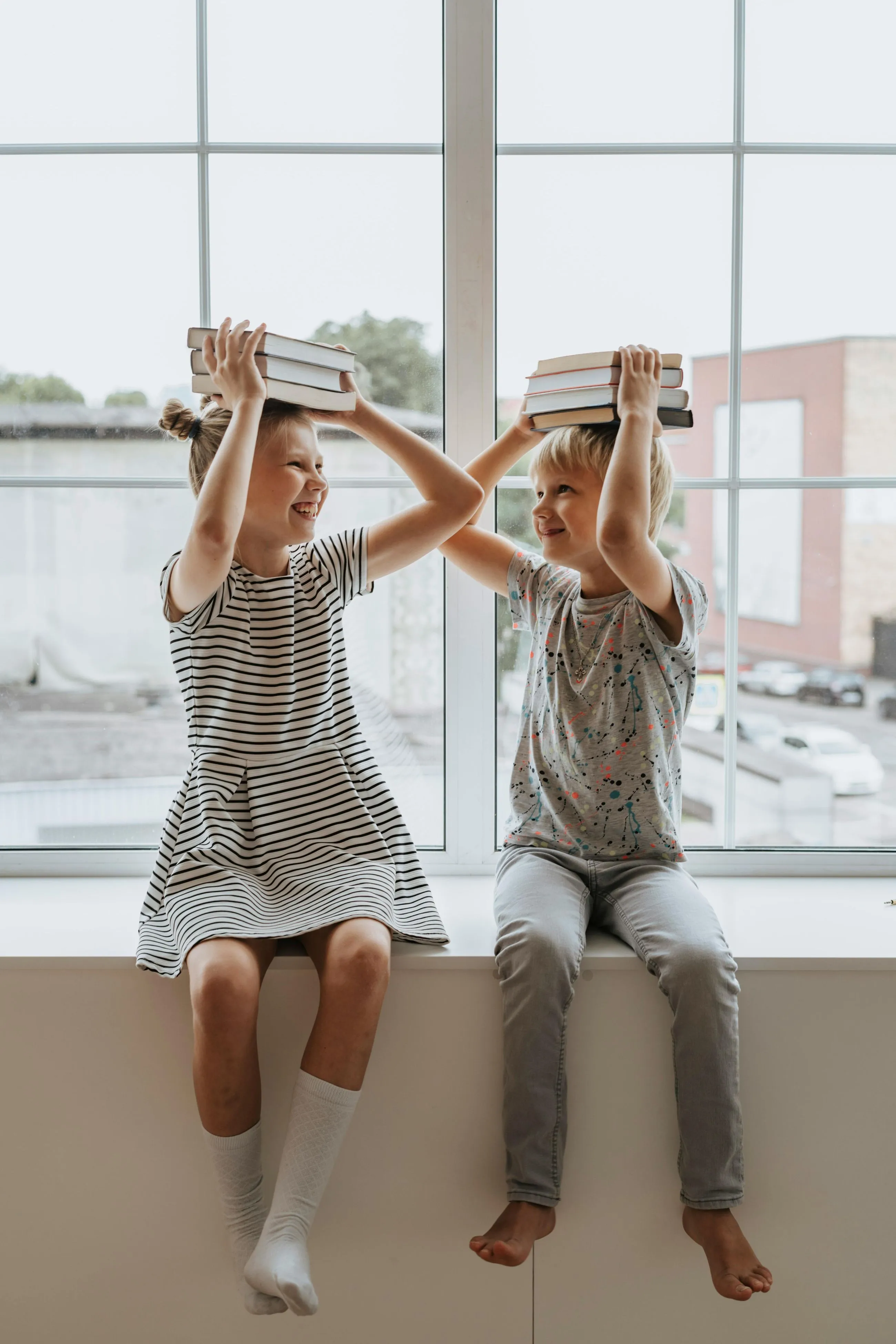 Two cheerful students are balancing books on their heads, smiling and laughing